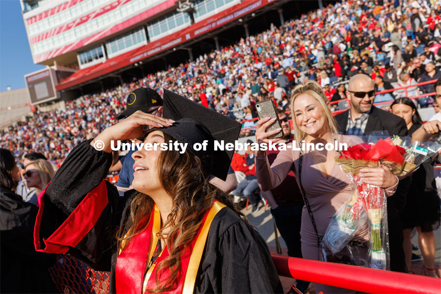 Angelique Fuentes squints into the sun as she tips her head back so her mother can photograph her decorated mortar board. Undergraduate commencement at Memorial Stadium. May 20, 2023. Photo by Craig Chandler / University Communication.