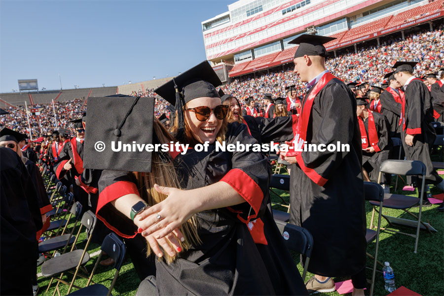 Madilyn Jaskae hugs Alisa Holst as part of Regent Tim Claire’s request that the graduates acknowledge each other with a hug, fist bump or hello. Undergraduate commencement at Memorial Stadium. May 20, 2023. Photo by Craig Chandler / University Communication.