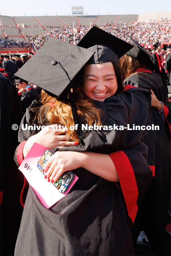 Olivia Kinne hugs Madilyn Jaskae as part of Regent Tim Claire’s request that the graduates acknowledge each other with a hug, fist bump or hello. Undergraduate commencement at Memorial Stadium. May 20, 2023. Photo by Craig Chandler / University Communication.