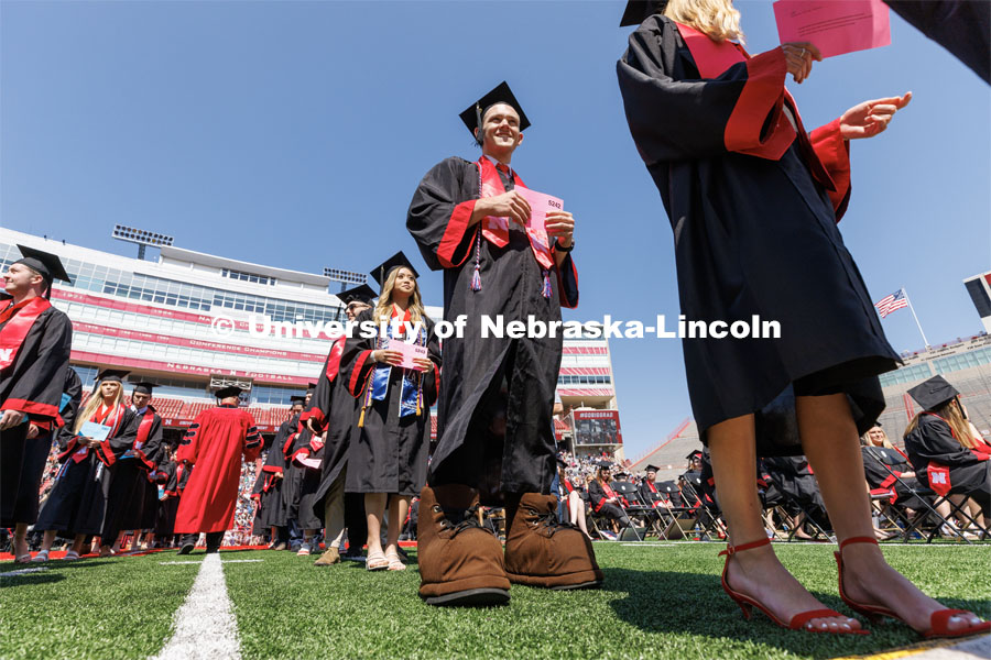 Brendan Kauth-Fisher, a graduate in business administration, waits in line to receive his diploma. Brendan has been seen by thousands the past three years performing as Herbie Husker. Herbies are allowed to reveal themselves at commencement by wearing Herbie’s shoes to walk. Undergraduate commencement at Memorial Stadium. May 20, 2023. Photo by Craig Chandler / University Communication.