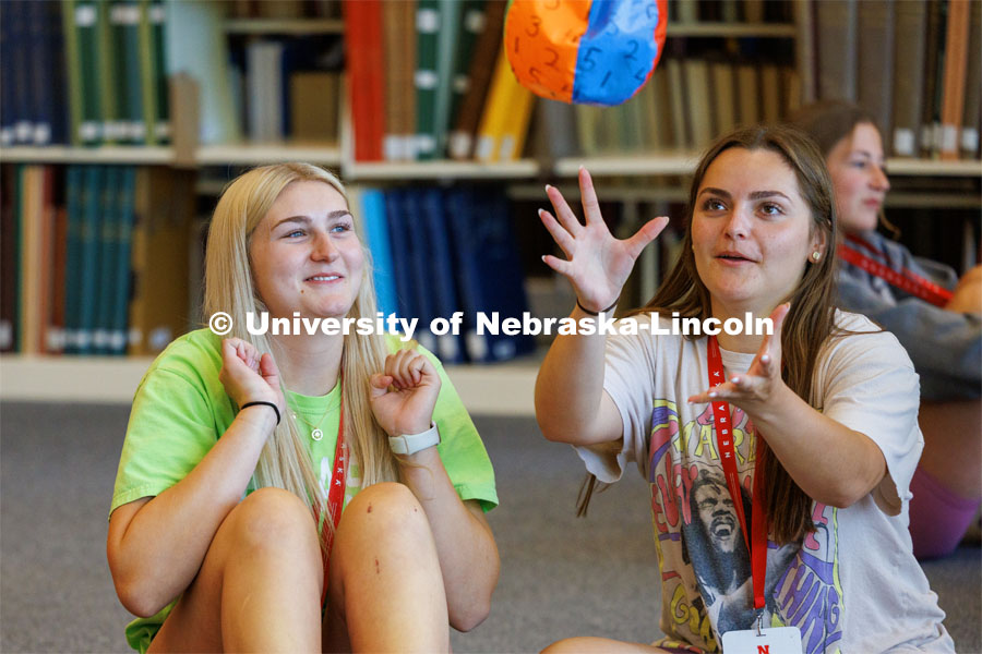Kennedy Malo of Lakeville, Minnesota, grabs a numbered beachball as Bradie Johnson of South Sioux City, Nebraska, pulls her arms back. After catching the ball, each NSE person answers a question about themselves depending on which number their right index finger touches. New Student Enrollment ( NSE ) on City Campus. June 13, 2023. Photo by Craig Chandler / University Communication.