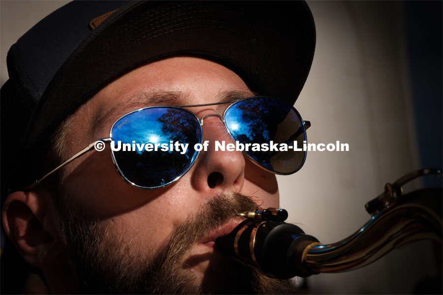 Sunset flares in the sunglasses of Christian Dahlman of Lincoln. The band practices on the greenspace by the Sheldon Art Museum as their normal pregame concert area next to the Kimball Recital Hall is under construction. Cornhusker Marching Band practice. August 16, 2023. Photo by Craig Chandler/ University Communication.