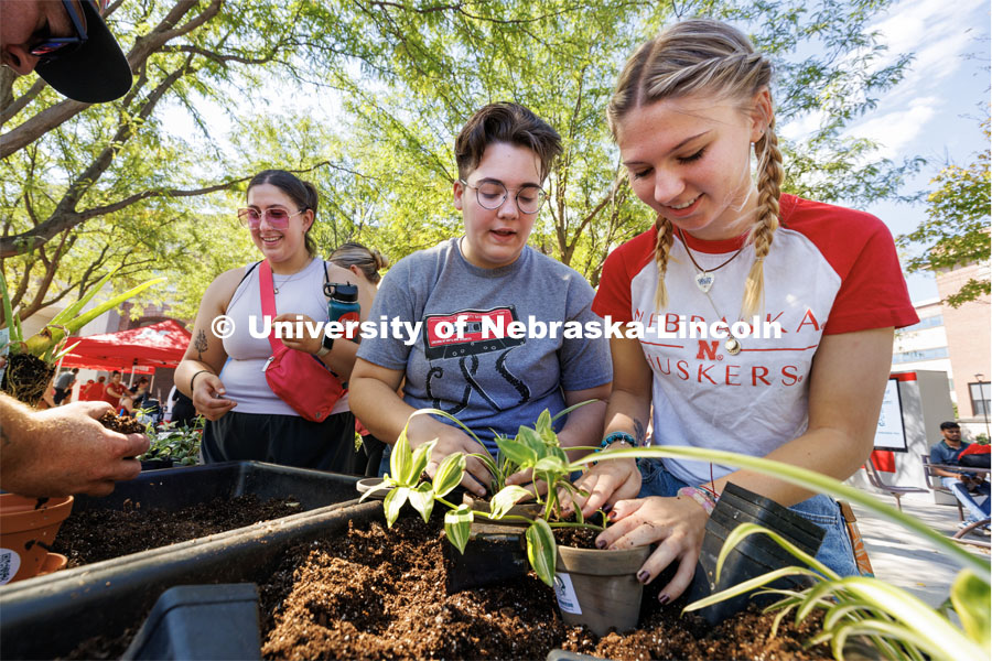 Shae Mitchell, a freshman from Edison, Nebraska, center, and Emmy Oldham, a freshman from Wellfleet, Nebraska, add potting soil for their plants being given away at Wellness Fest. At left, Olivia Hanson, a freshman from East Moline, Illinois, awaits her plant. August 19, 2023. Photo by Craig Chandler / University Communication.