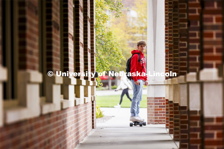 Raikes student skateboarding through the outdoor corridors of the Kauffman Academic Residential Center on their way to class. Raikes School photo shoot. October 18, 2023. Photo by Craig Chandler / University Communication.