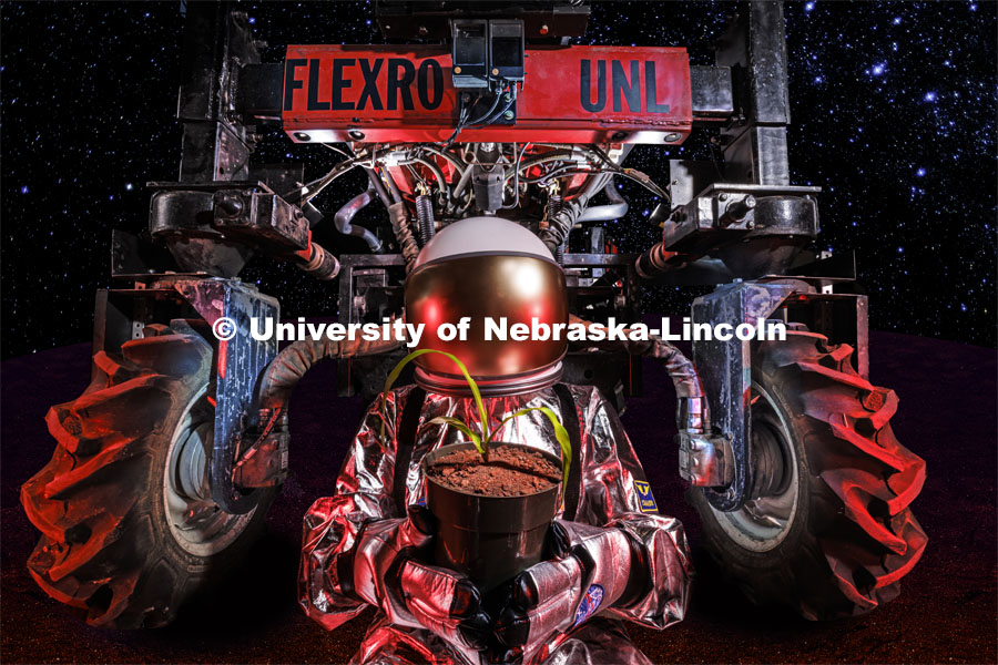 An “astronaut” holds a small corn plant with the Flex-Ro autonomous planter behind her. A planter for Mars would be much smaller so it can be transported easier and also because the “fields” would probably be in enclosed spaces. Photo illustration for Space 2, the Nebraska Grand Challenge led by professors in Biological Systems Engineering to grow crops on Mars. October 20, 2023. Photo by Craig Chandler / University Communication.