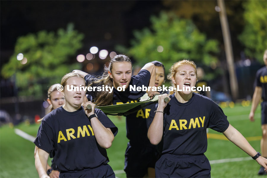 Army cadet Natalie Karrek rides the litter during the casualty evacuation race carried by, clockwise from front center, Rianna Wells, Michaela Guzman, Alyssa Batista and Grace Charlesworth. Cadet Remy Abdulahi shouts encouragement as the team races around the soccer field on Mabel Lee fields. Each branch ran a timed 220 yard race for the male and female cadets and midshipman. ROTC Joint Field Meet is like an ROTC Olympics for the Nebraska cadets and midshipman. Army, Air Force and Navy/Marine cadets compete in events such as Maneuvering Under Fire, Log Sit-ups, Tug-Of-War, Casualty Evacuation and Ultimate Frisbee. Army beat Navy in a sudden death 4x400 relay to claim the title. October 26, 2023. Photo by Craig Chandler / University Communication.
