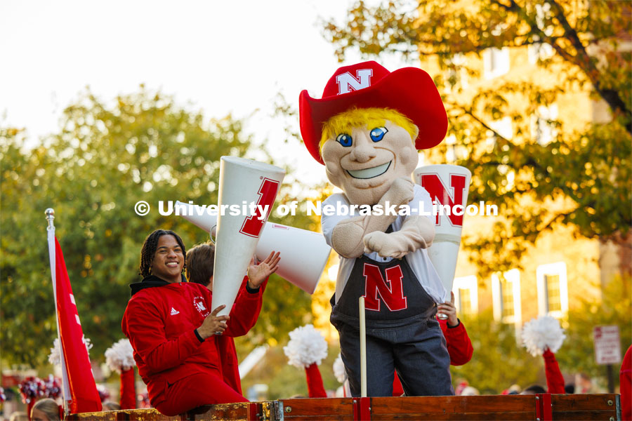 Herbie Husker and Amani Mfinanga cheer from a tractor-pulled wagon in the Homecoming parade. October 27, 2023. Photo by Craig Chandler / University Communication.