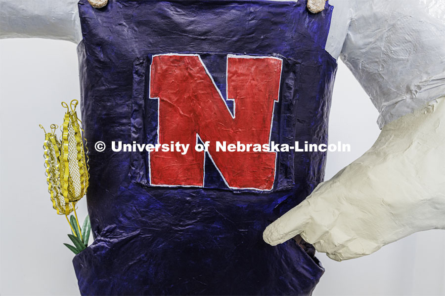 Ears of corn stick out of the pocket of the papier mâché Herbie. Dohe, Administrative Coordinator for Electrical and Computer Engineering, has made an 8-foot tall Herbie Husker from paper- mâché. She hopes to auction it off to help veterans. October 30, 2023. Photo by Craig Chandler / University Communication.