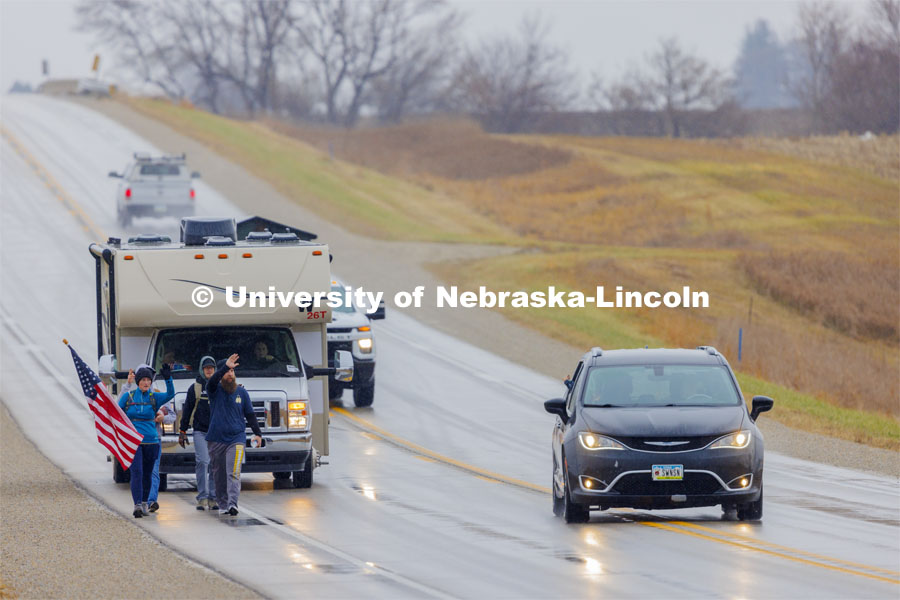 Iowa veterans Dawn Walton and Casey Swanson wave to a passing car as they walk with their group along Hwy 83 east of Atlantic, Iowa, carrying the Nebraska v. Iowa game ball. The Things They Carry" ruck march involving military and veteran students from Iowa and Nebraska. To raise awareness about veteran suicide, through the week, the students walk in 20-mile shifts carrying 20-pound backpacks to commemorate the estimated 20 veterans who die by suicide each day. November 20, 2023. Photo by Craig Chandler / University Communication and Marketing.