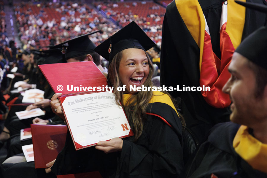 Allison Aden shows off her new diploma to family and friends after returning to her seat. Graduate Commencement at Pinnacle Bank Arena. December 15, 2023. Photo by Craig Chandler / University Communication and Marketing.