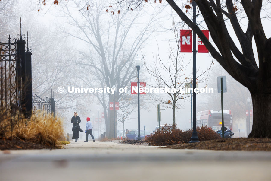 Students cross campus near the Love Garden gates on a foggy morning on City Campus. February 5, 2024. Photo by Craig Chandler / University Communication and Marketing.