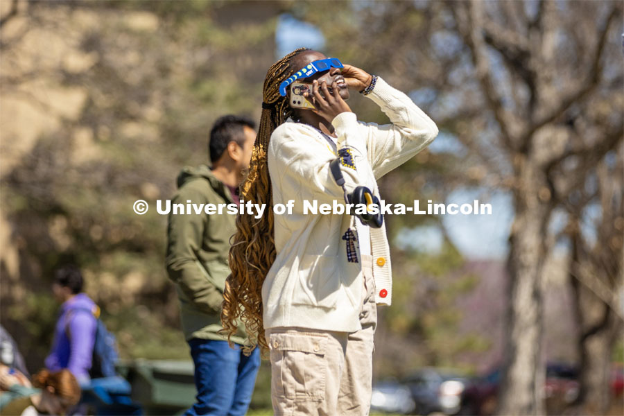 A student catches a glimpse of the eclipse as she talks on the phone on East Campus. April 8, 2024. Photo by Kristen Labadie / University Communication.