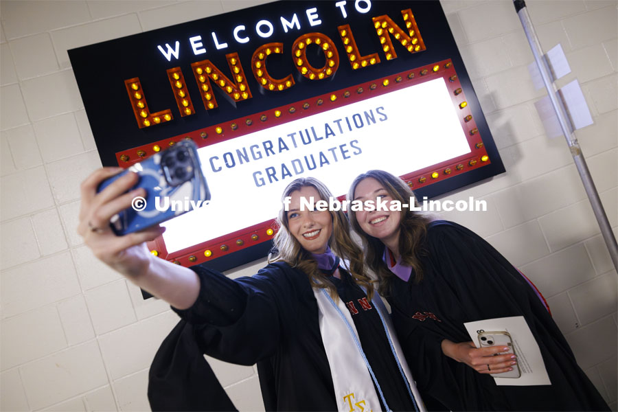 Kathleen O’Gara and Sophia Swanson take a selfie in front of a marquee in the hallways in Pinnacle Bank Arena. Graduate Commencement. May 17, 2024. Photo by Craig Chandler / University Communication and Marketing.