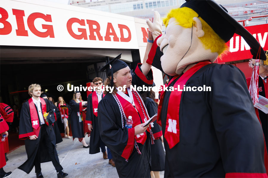 Caleb Pruss-Hansen high-fives Herbie Husker as the graduates enter the field. Undergraduate Commencement in Memorial Stadium. May 18, 2024. Photo by Craig Chandler / University Communication and Marketing.