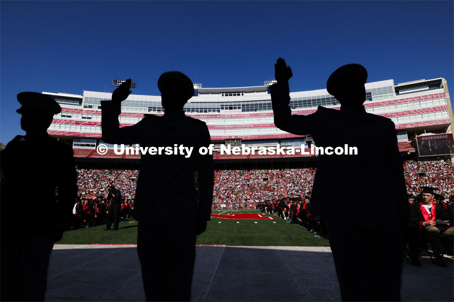 Marine Second Lieutenant Dane Bowers and Navy Ensigns Peyton Weigand and Kenneth Reese are silhouetted against the west stadium as they recite their ROTC oath. Undergraduate Commencement in Memorial Stadium. May 18, 2024. Photo by Craig Chandler / University Communication and Marketing.