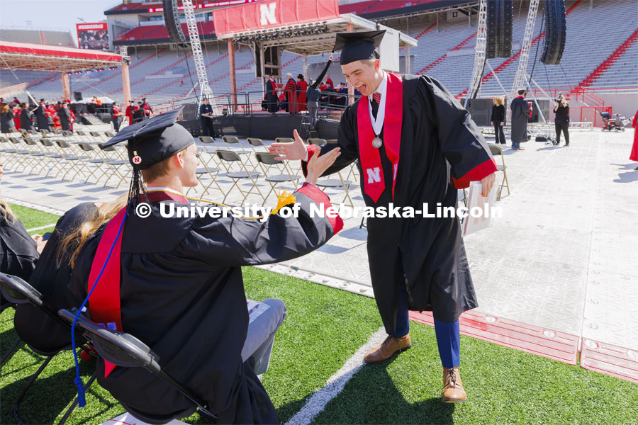 Harrison Wells, standing, and Trenton Sedlacek congratulate each other after Wells received his diploma. Undergraduate Commencement in Memorial Stadium. May 18, 2024. Photo by Craig Chandler / University Communication and Marketing.