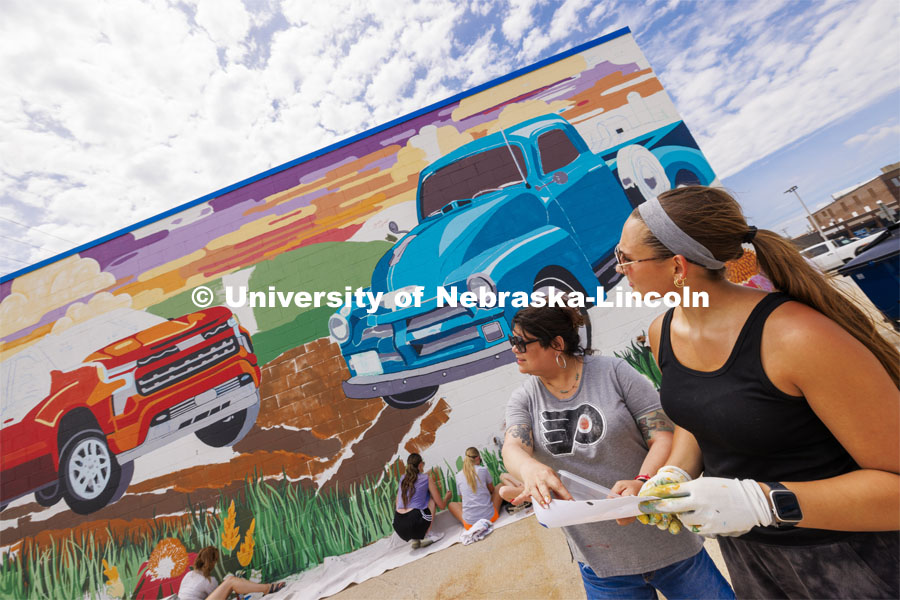 Sandra Williams, center, and Maddie Vanderbur, a senior in graphic design and the mural’s designer, look over a printout of the mural. ARTS 398 - Special Topics in Studio Art III taught by Sandra Williams. The class painted a mural at the Premier Buick, Chevrolet, and GMC dealership in Beatrice. June 3, 2024. Photo by Craig Chandler / University Communication and Marketing.