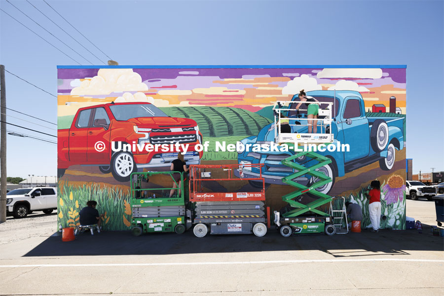 The class works high and low using a scissor lift on the final touches for the mural. ARTS 398 - Special Topics in Studio Art III taught by Sandra Williams. The class painted a mural at the Premier Buick, Chevrolet, and GMC dealership in Beatrice. June 6, 2024. Photo by Craig Chandler / University Communication and Marketing.