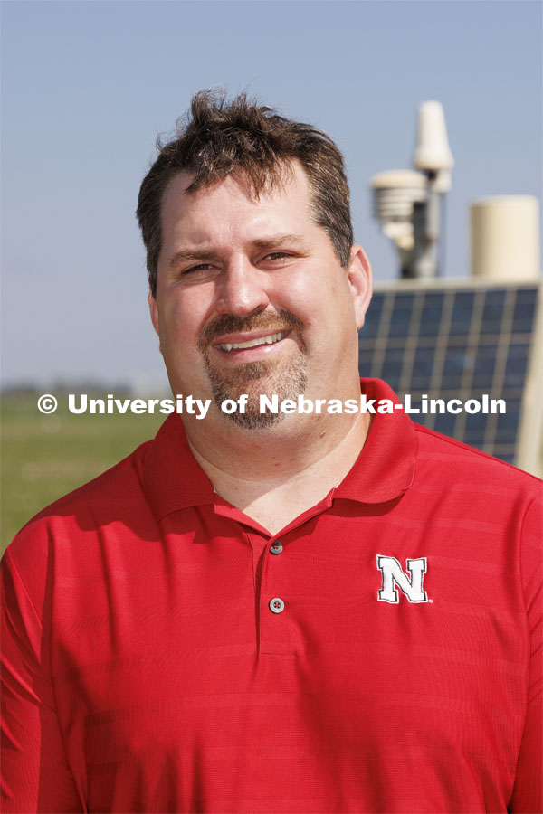 Trenton Franz poses in front of one of the cosmic ray neutron sensors at the edge of a field at the Eastern Nebraska Research, Extension and Education Center (ENREEC) near Mead, Nebraska. The sensors' readings indicate soil moisture levels. Solar flares, such as those that produced the auroras in Nebraska on May 10-11, trigger electromagnetic interference in the sensors' readings. UNL has taken steps to correct the distortions and ensure data reliability. Franz is using neutron and cosmic ray detectors to see how solar radiation and solar energy such as those that caused Nebraska to view the Northern Lights is effecting precision farming including soil moisture detectors and the GPS in tractors. June 21, 2024. Photo by Craig Chandler / University Communication and Marketing.