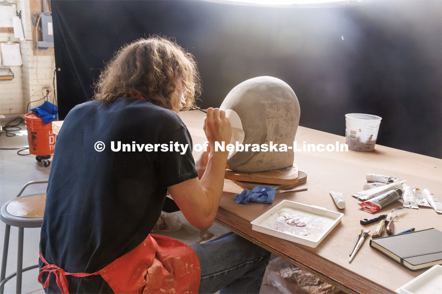 Dawson Adams, a sophomore art student, paints on his sculpture head. Behind the scenes photo for the university's new "Home Again" national advertisement. June 25, 2024. Photo by Kristen Labadie / University Communication.