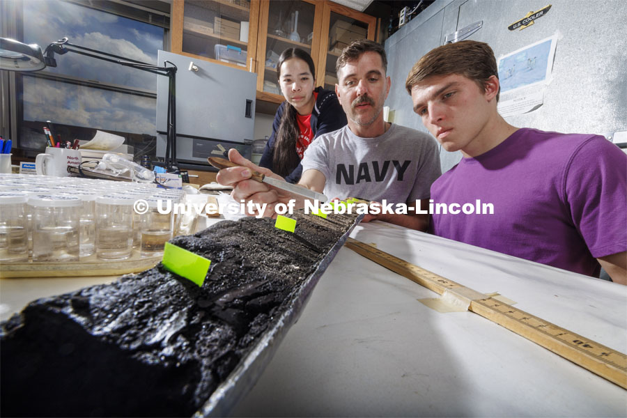 Doctoral student Jim Benes points out the layers of soil deposited in a core sample from Nebraska’s sandhills with UCARE students Jasmine Pham, left, and Joe Stalder. These charcoal samples help tell the history of fire in the Sandhills. Benes, a geography Ph.D. student in the School of Global Integrative Studies, works in the same Bessey Hall lab he worked in as an undergrad. July 18, 2024. Photo by Craig Chandler / University Communication and Marketing.