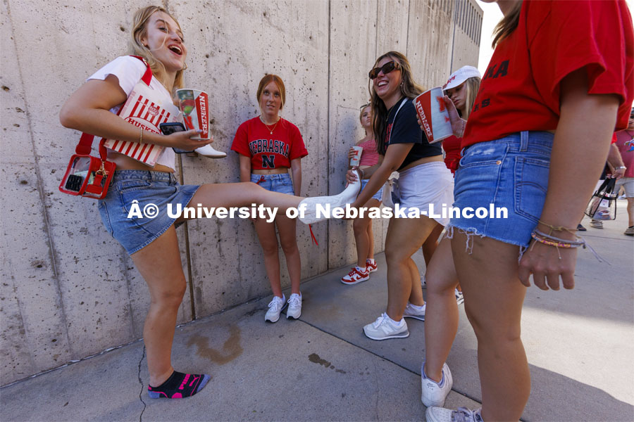 One student helps another remove her boots at the Nebraska football game vs UTEP. August 31, 2024. Photo by Craig Chandler / University Communication and Marketing