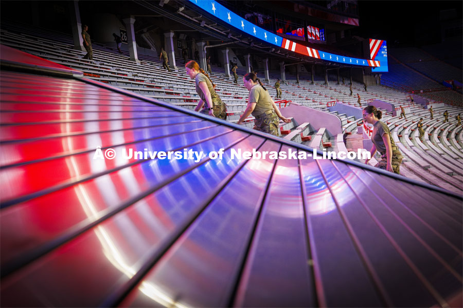 Army ROTC cadets Michaela Guzman, Chloe Johnston and Ella Valleley climb the steps in Memorial Stadium as red, white and blue electronic graphics are reflected across a stairwell cover. 9/11 stair climb in Memorial Stadium to commemorate September 11, 2001. September 11, 2024. Photo by Craig Chandler / University Communication and Marketing.