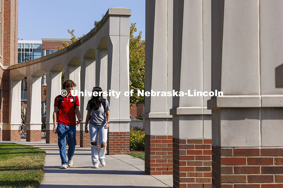 Raikes School students Gannett Bishop and Nina Glick walk along the columns outside of the Kauffman Academic Residential Center. Raikes School photoshoot. October 9, 2024. Photo by Craig Chandler / University Communication and Marketing.