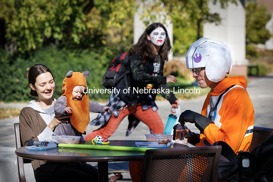 On a lunch table far far away, Alejandra Semadeni (left) young Ewok, (Melinda) and Steven Semadeni eat lunch outside the Nebraska Union as a ghoul rolls by in the background. Halloween on Campus. October 31, 2024. Photo by Craig Chandler / University Communication.