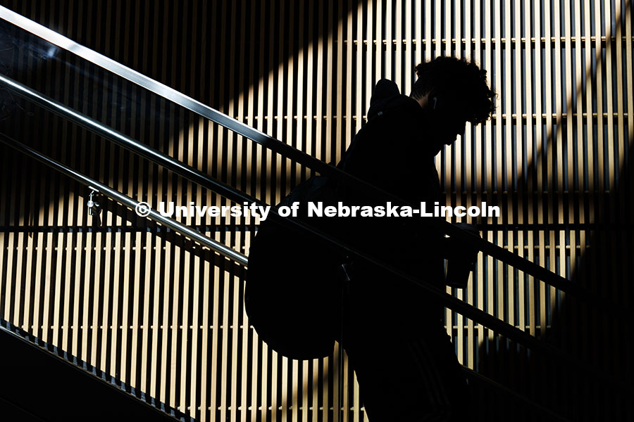 A student is silhouetted as sunlight shines on the wall behind them as they walk downstairs in the College of Business. City Campus. November 12, 2024. Photo by Jordan Opp / University Communication and Marketing.