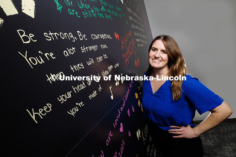 Gina May, Project SAFE clinical coordinator and graduate student, stands next to a wall containing inspirational messages inside the BraveBe Child Advocacy Center written by adolescent and teenaged clients. November 18, 2024. Photo by Jordan Opp / University Communication and Marketing.