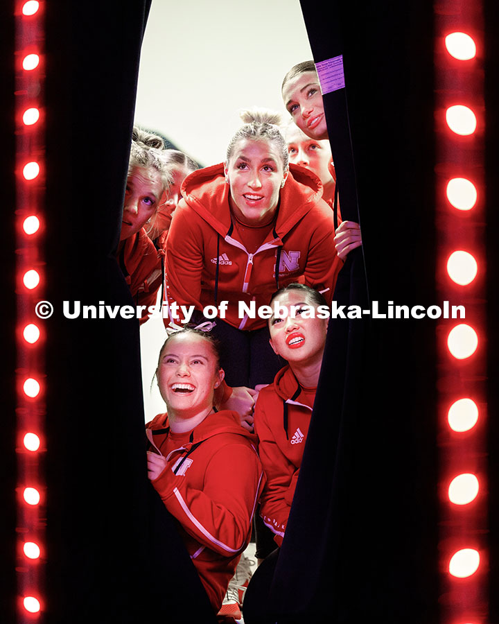 Members of the women’s gymnastics team peak through a curtain to watch their hype video before the