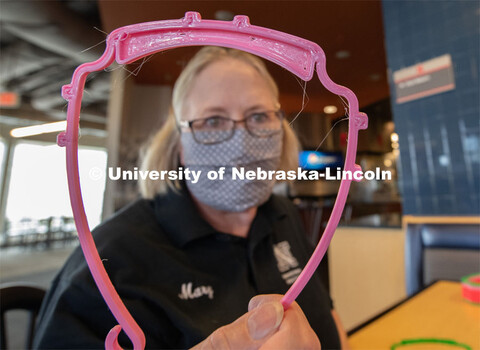 Janet Nichols holds up a face shield frame. Dinning Services employees, Rochan Pinho, Janet Nichols 