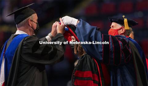 Caitlin Coulson is hooded by Professor Galen Erickson and Tim Carr, Associate Vice Chancellor and De