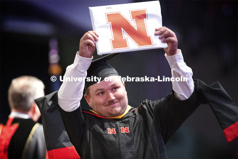 Ely Anderson holds up his masters diploma to friends and family in the arena. Summer Graduate Commen