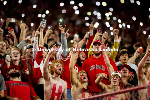 Fans with HUSKERS painted on their chests hold up their cell phone flashlights to light up the stand