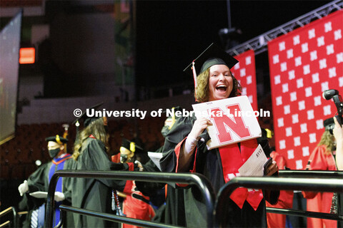 A new grad holds up her diploma and smiles for the camera at the Undergraduate Commencement at Pinna