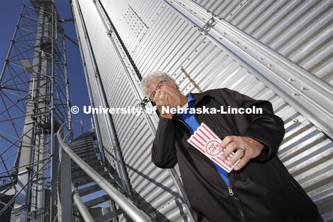 Husker alumnus Norm Krug enjoys a handful of Preferred Popcorn standing at the base of a grain bin o