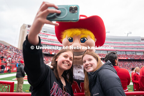 Freshmen Emma Georgia, left, and Bethany Dvorachek take a selfie with Herbie Husker during the sprin