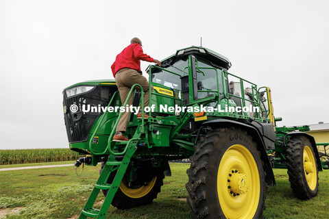 Chancellor Rodney Bennett climbs up on a John Deere sprayer that uses cameras and computers to only 