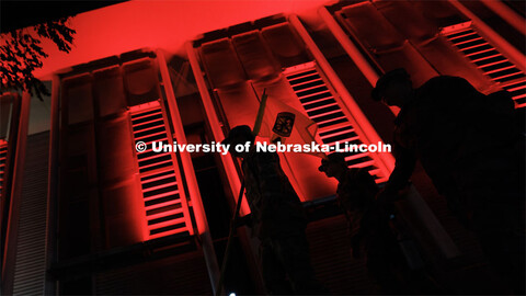 Army ROTC cadets carry their guidon past the red-lighted Schorr Center as they head into the stadium