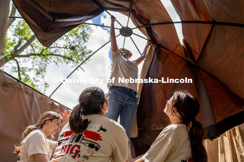 Members of Tri Delta hold a ladder steady while Rachel Nelson pulls the roof of a pergola over the t