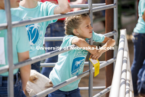 A young girl holds her yellow ribbon while watching the activities through a fence. 4-H Polk County 