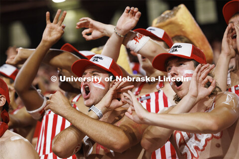 Cheering fans throwing the bones in the student section wear red and white striped overalls. Nebrask