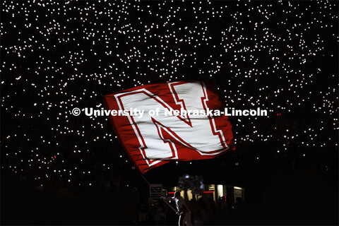 Husker Cheer Squad member Jake Seip waves the Nebraska flag during the end-of-third-quarter light sh