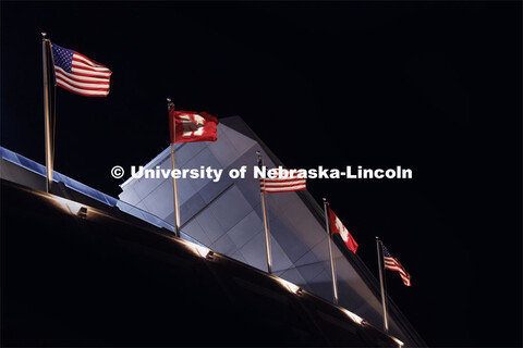 Flags on the top of Memorial Stadium are illuminated in the night sky at the Nebraska vs. Illinois f