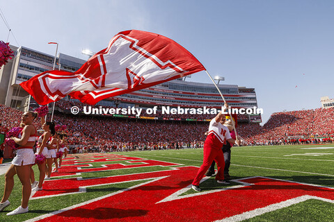 Husker Cheer Squad member Jake Seip fights the high wind speeds with Herbie Husker’s help as he tr