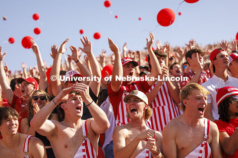 Cheering fans in the student section wear red and white striped overalls. Nebraska vs Rutgers footba