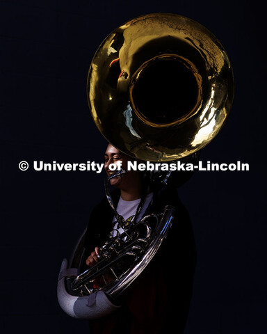 A member of the Cornhusker Marching Band carries their sousaphone and smiles as they walk out of Mem