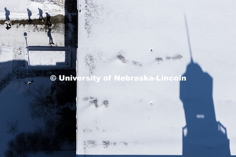 Aerial view of students crossing campus in the snow with the shadow Love Library’s cupola reflecte